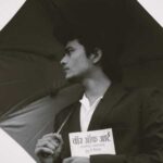 Black and white photo of a man in a suit holding an umbrella and a book, exuding elegance and mystery., tags: hyphen übersetzt indische und sie einem - pexel