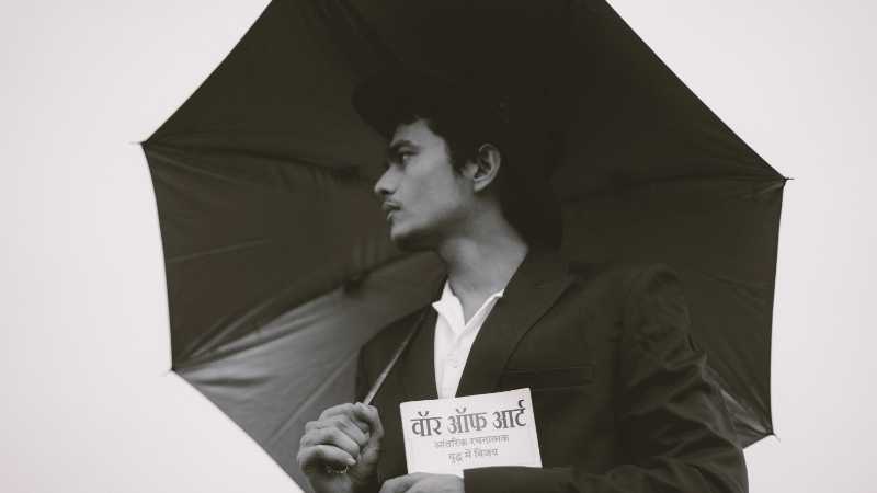 Black and white photo of a man in a suit holding an umbrella and a book, exuding elegance and mystery., tags: hyphen übersetzt indische und sie einem - pexel